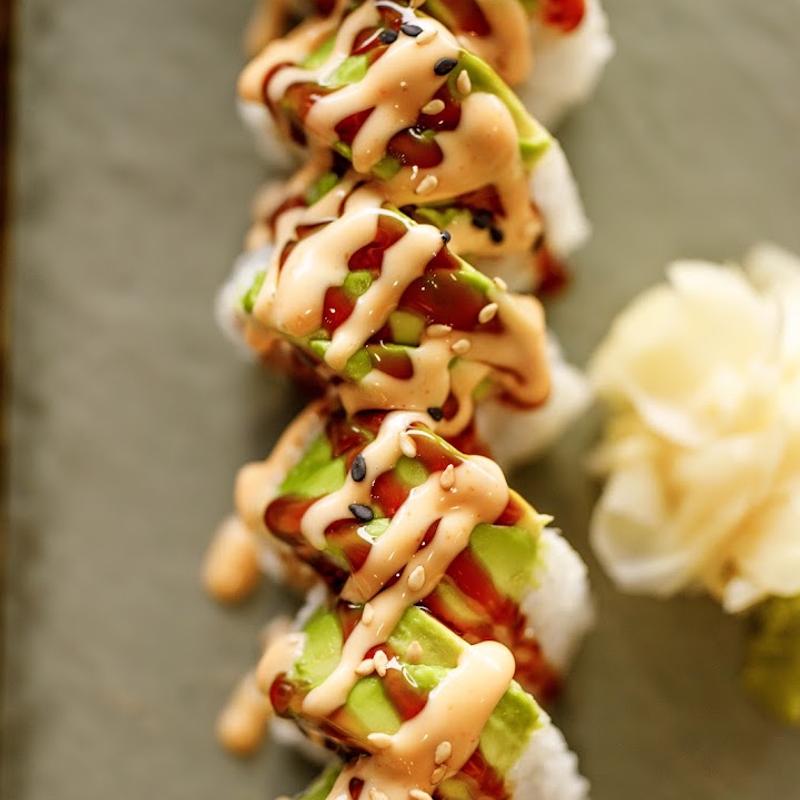 Sushi roll topped with sliced avocado, spicy mayo and eel sauce, overhead view.