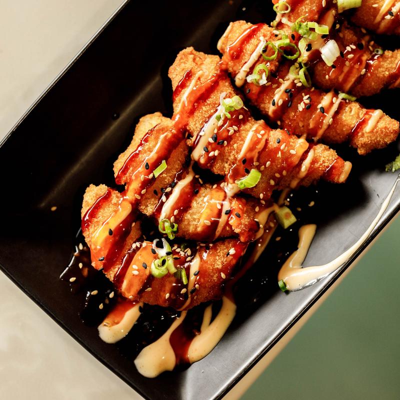Fire Cracker Shrimp served on a black plate and drizzled with sauces.